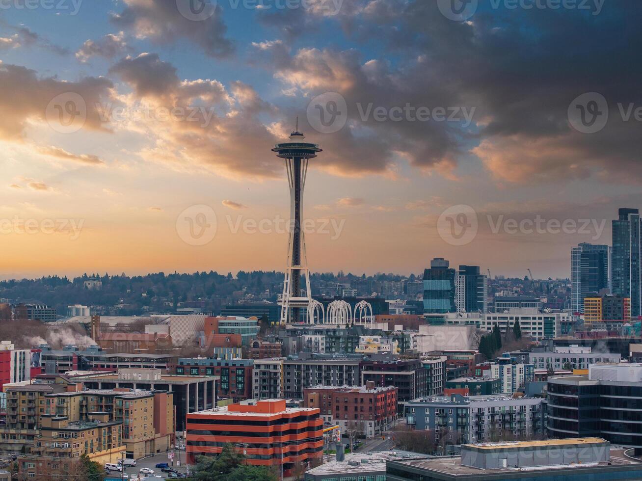 Downtown Seattle's skyline with the Space Needle at the center, surrounded by modern and historic buildings, greenery, and a warm sunset sky. photo