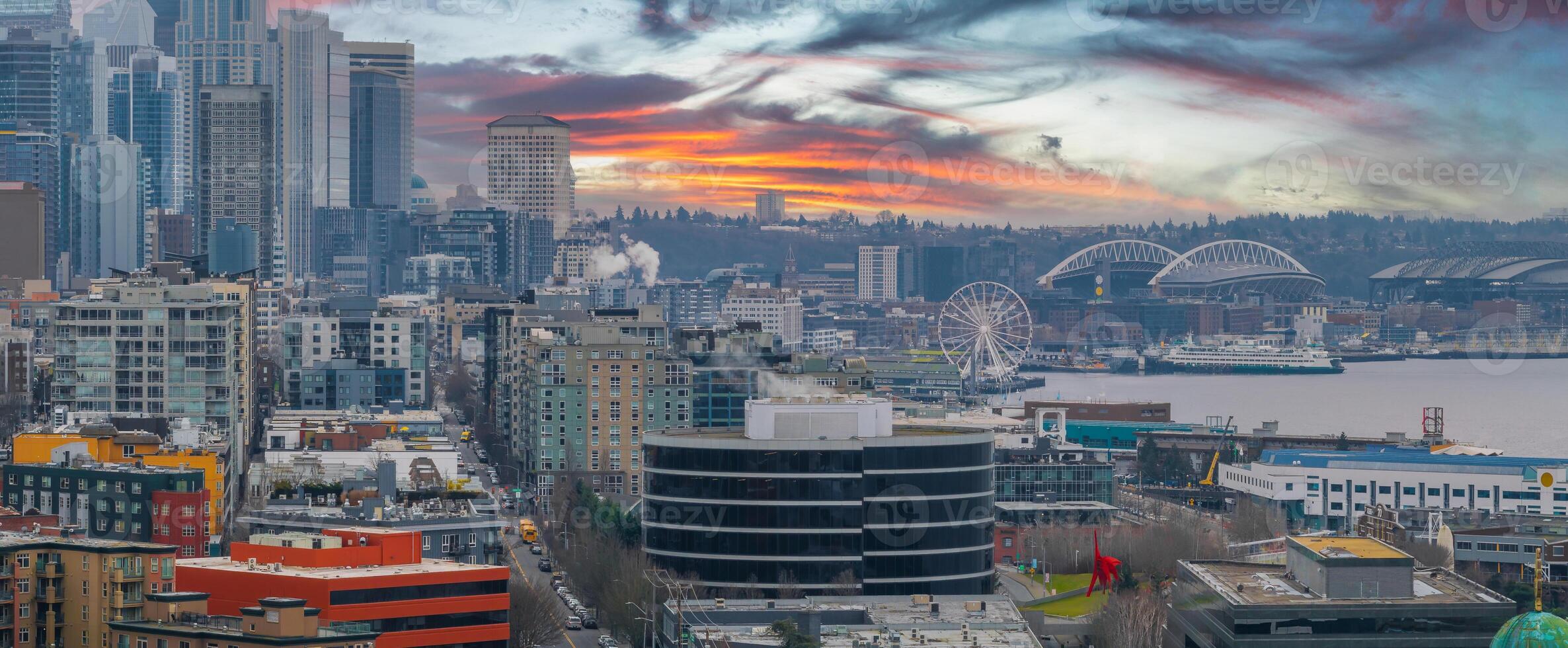 Aerial view of downtown Seattle, Washington, featuring skyscrapers, the Seattle Great Wheel, Lumen Field, T Mobile Park, and a cargo ship in Elliott Bay. photo