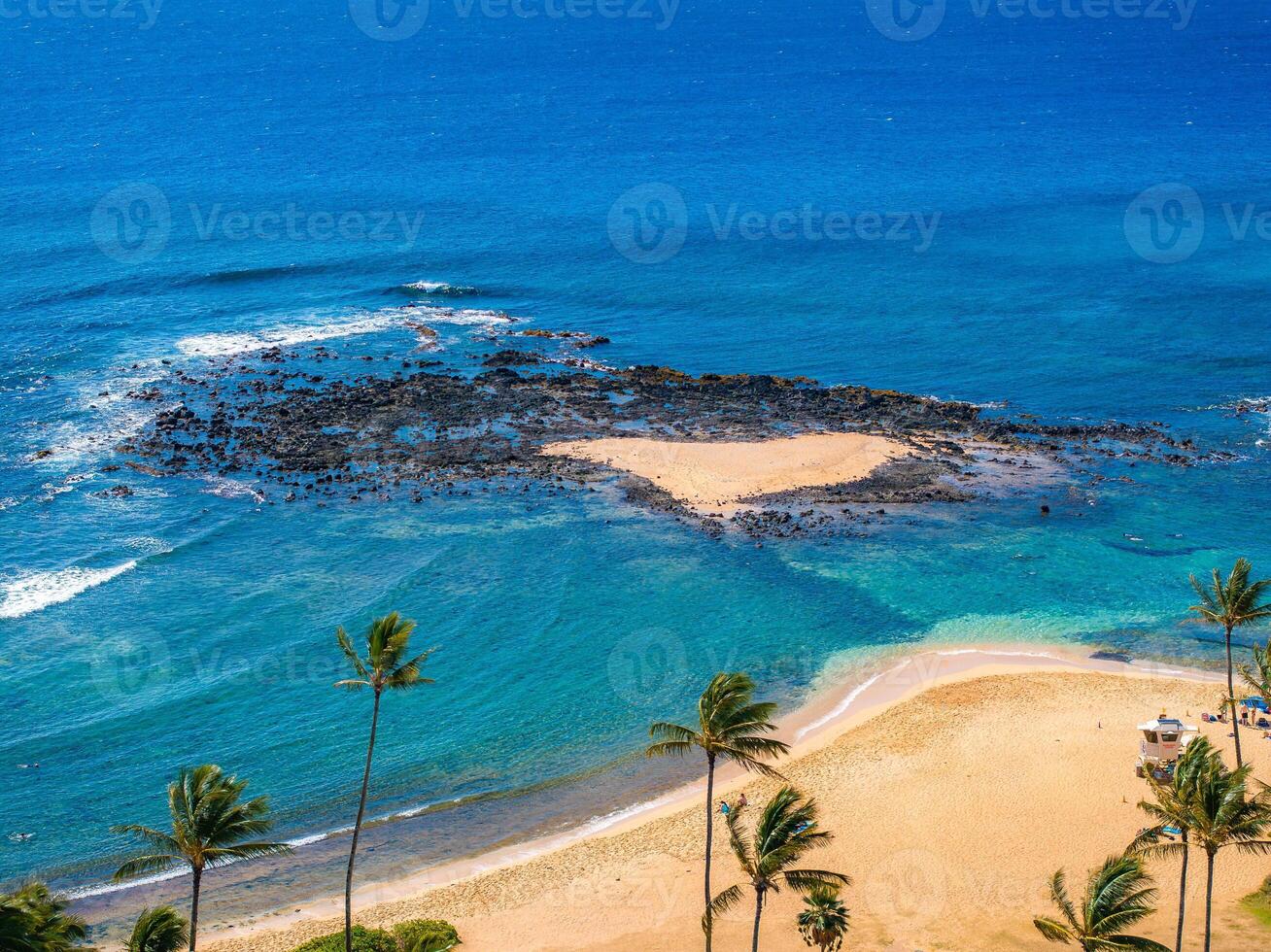 Aerial view of a Kauai beach in Hawaii featuring a heart shaped sandbar, volcanic rocks, turquoise waters, palm trees, and a lifeguard station. photo