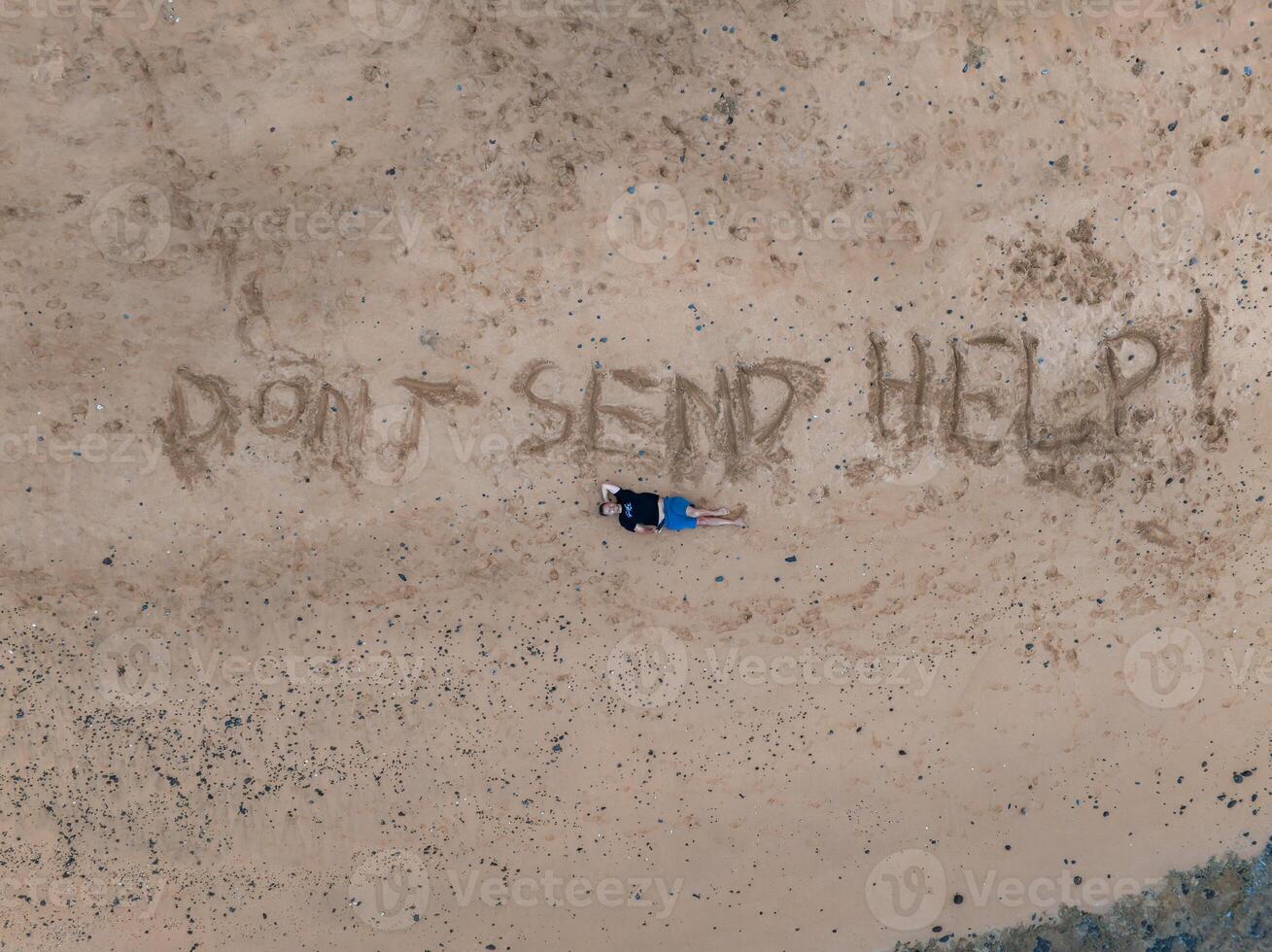 An aerial view of a sandy beach on Kauai island featuring the phrase 'DON'T SEND HELP ' written in the sand, with a person lying nearby. photo
