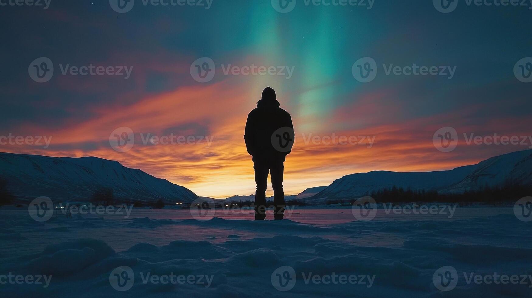 A person standing in the snow at sunset with the aurora borealis photo