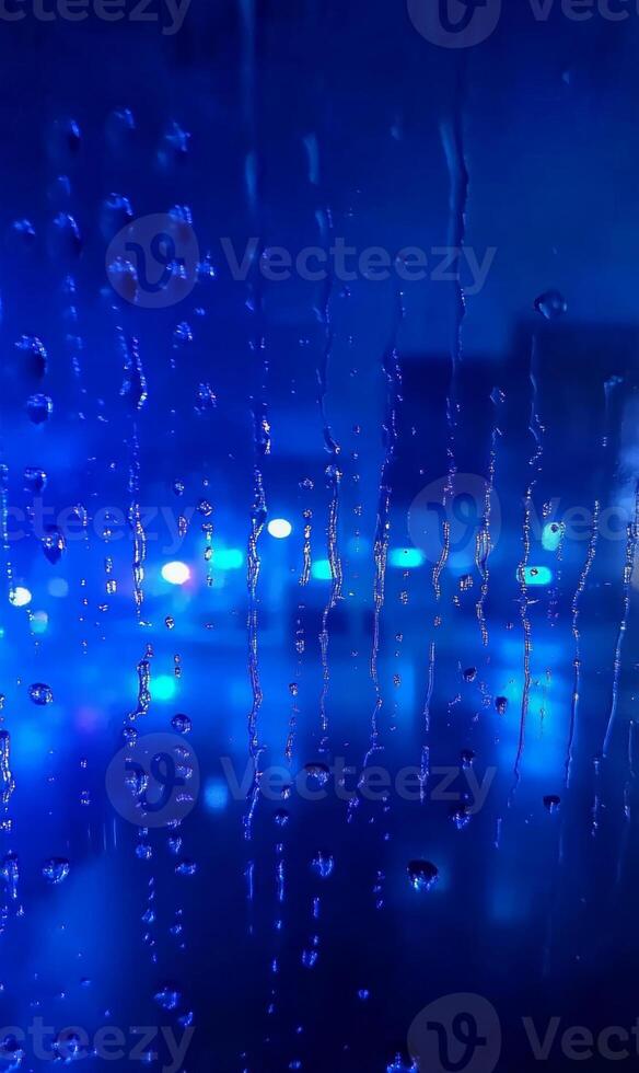 Electric twilight behind rain streaked window, cobalt blurred city lights through condensation photo