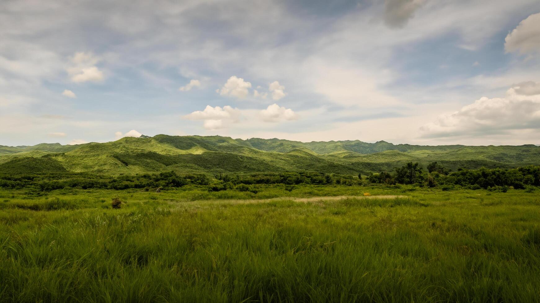 Lush green field, rolling hills, cloudy sky, rural landscape, travel postcard photo