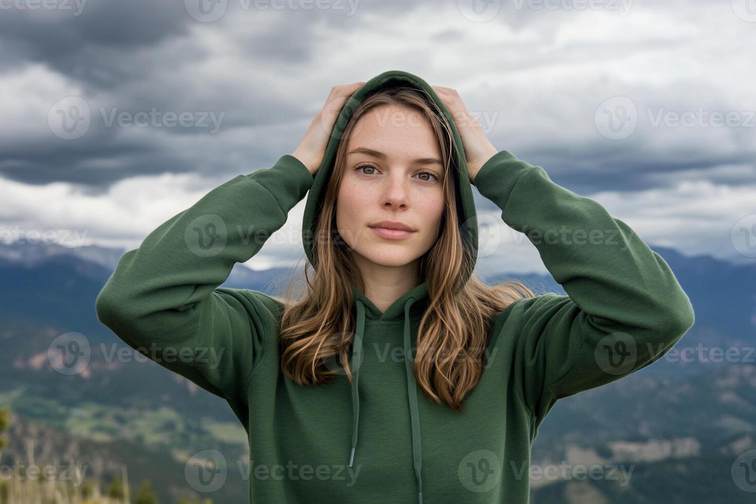 Woman in hoodie, mountain backdrop, serious expression. Possible use stock photo