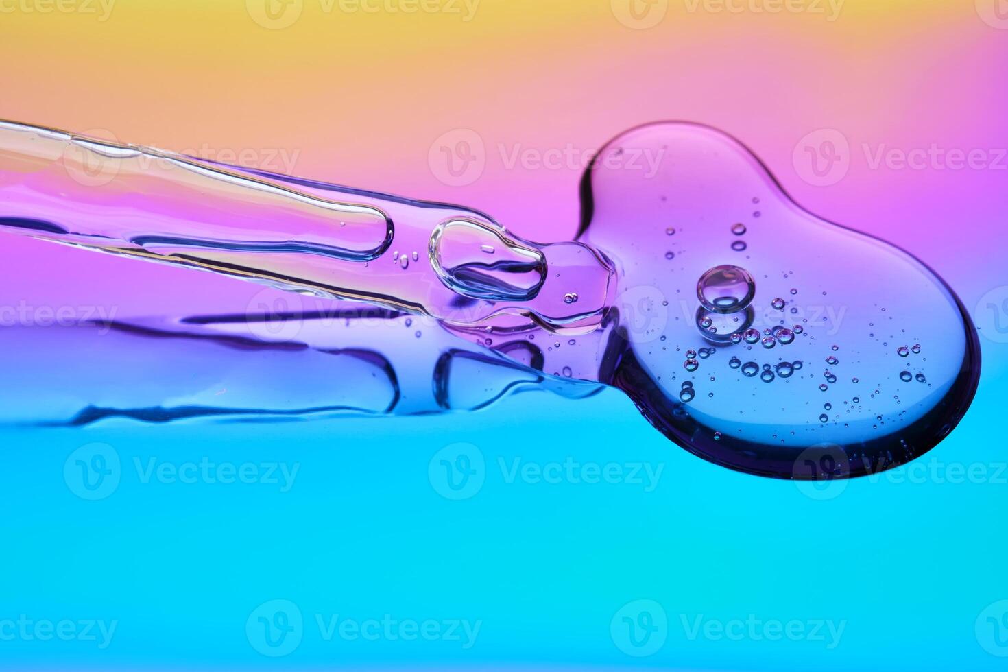 A drop of cosmetic serum and a pipette on a multicolored background in shades of blue and lilac. photo