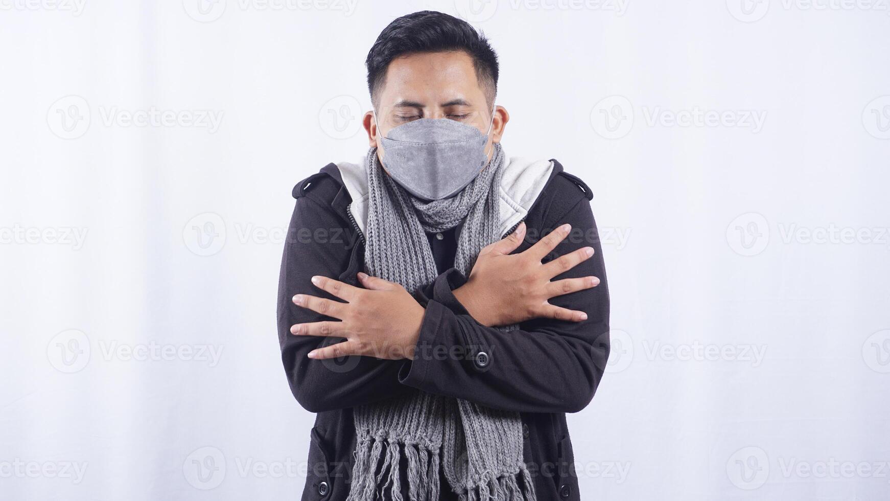 Unhealthy Asian Man Wearing Mask and Scarf Feeling Chills on White Background photo