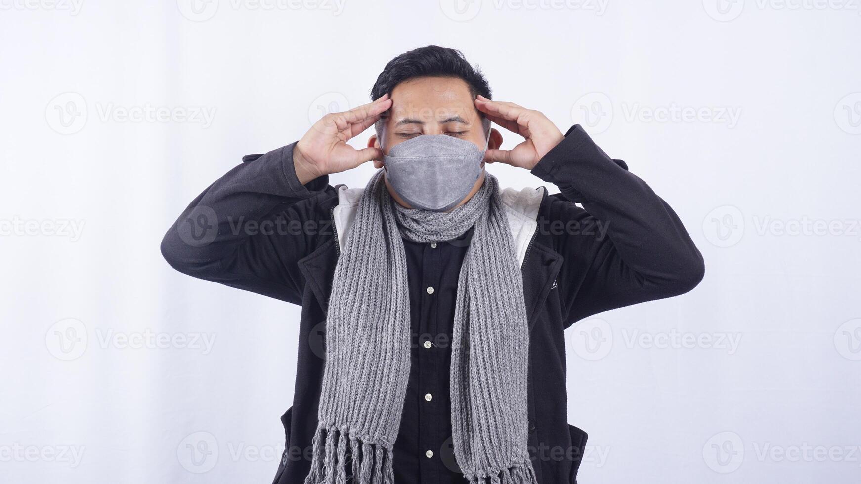 Asian Man Wearing Jacket, Scarf, and Mask Feels Headache on White Background photo