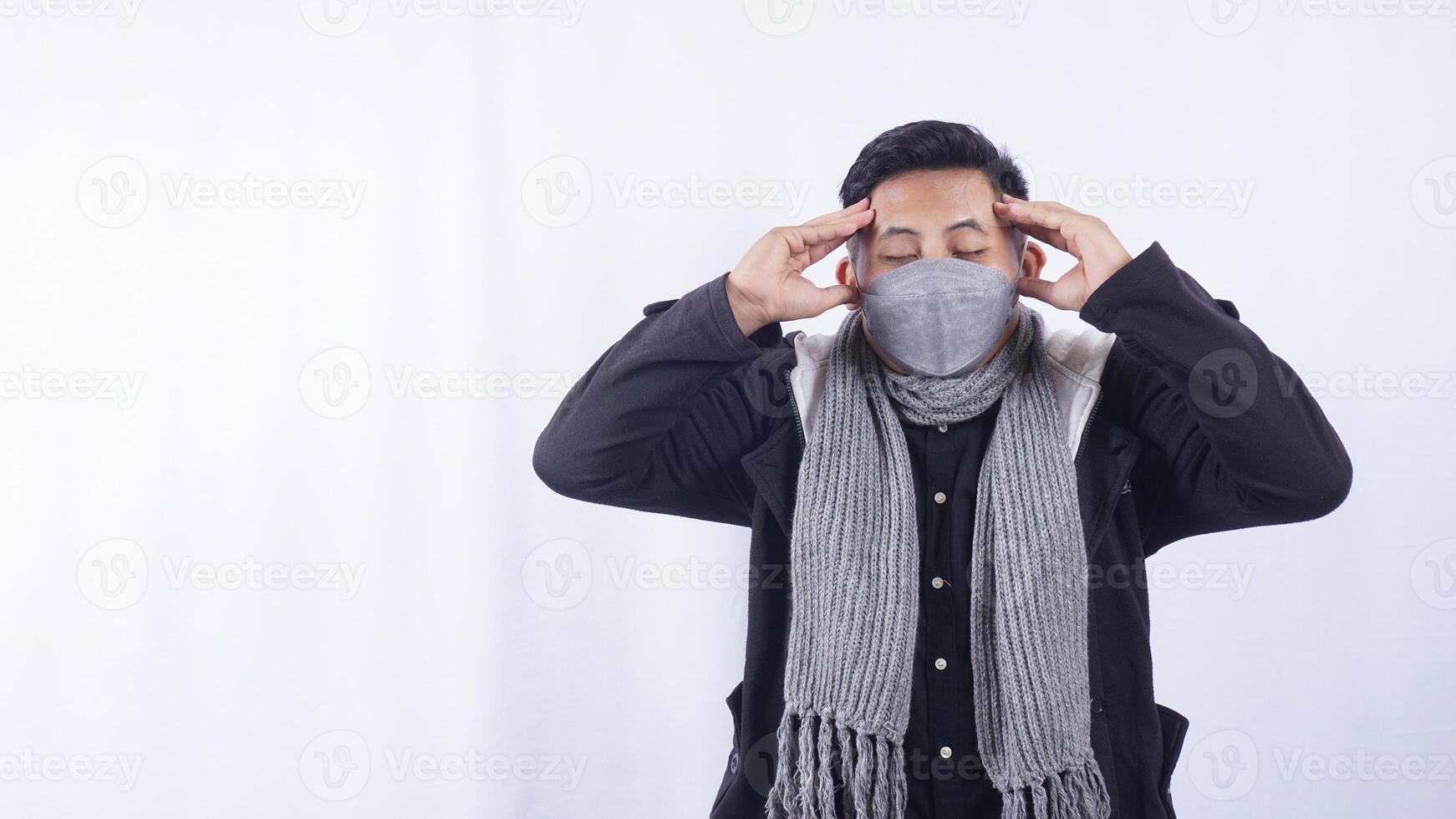 Asian Man Wearing Jacket, Scarf, and Mask Suffering from Bad Headache on White Background photo