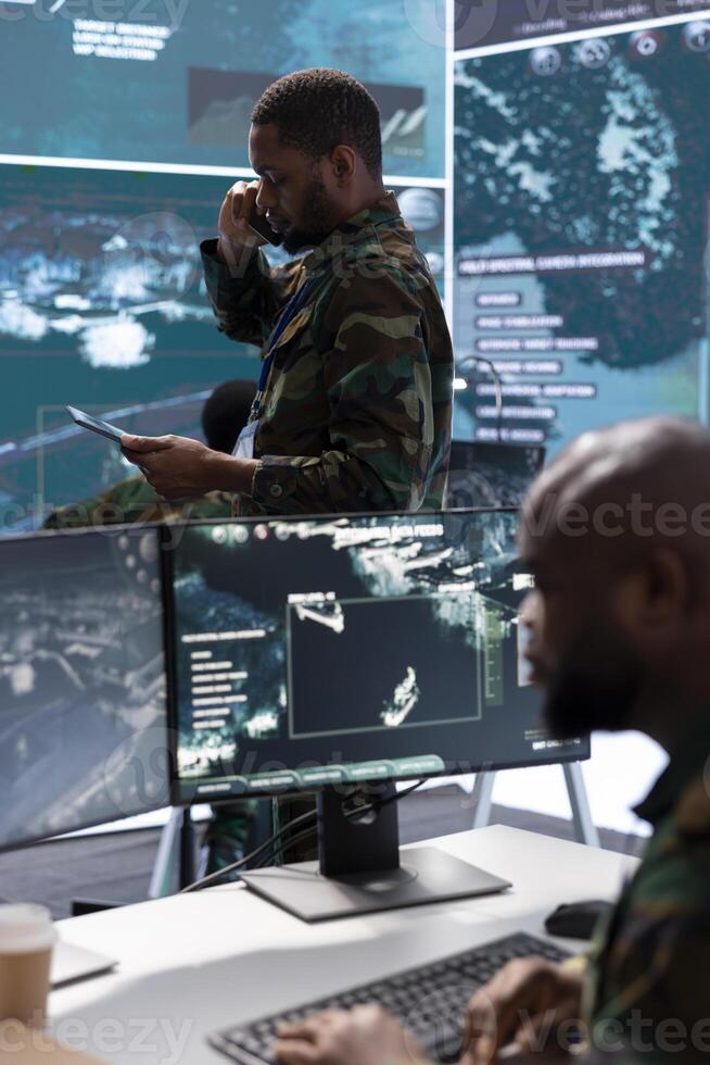 Soldier discussing on phone call in a modern control room, processing real time data and coordinating surveillance efforts. Enhancing national security by supporting decision-making processes. photo