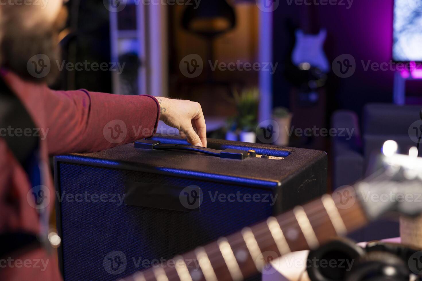Sound engineer adjusting volume levels on his amplifier to record acoustic guitar tunes for editing session in music post production. Male producer composing a new song in home studio. Close up. photo
