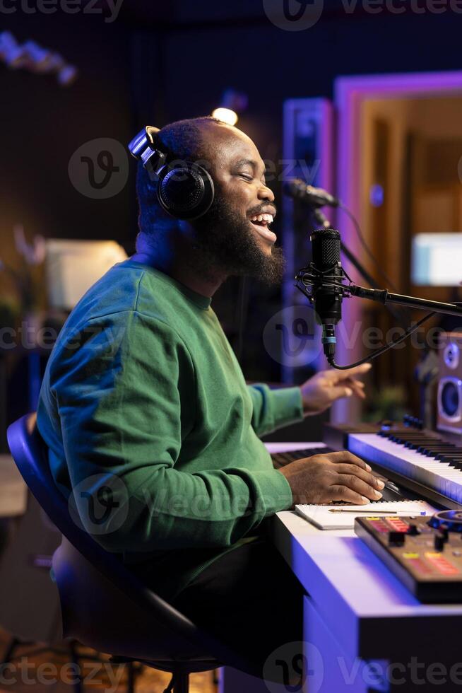 African american singer recording an acoustic version of his song, recording new music on microphone. Skilled artist composer uses stereo gear to launch new soundtracks in home studio. photo