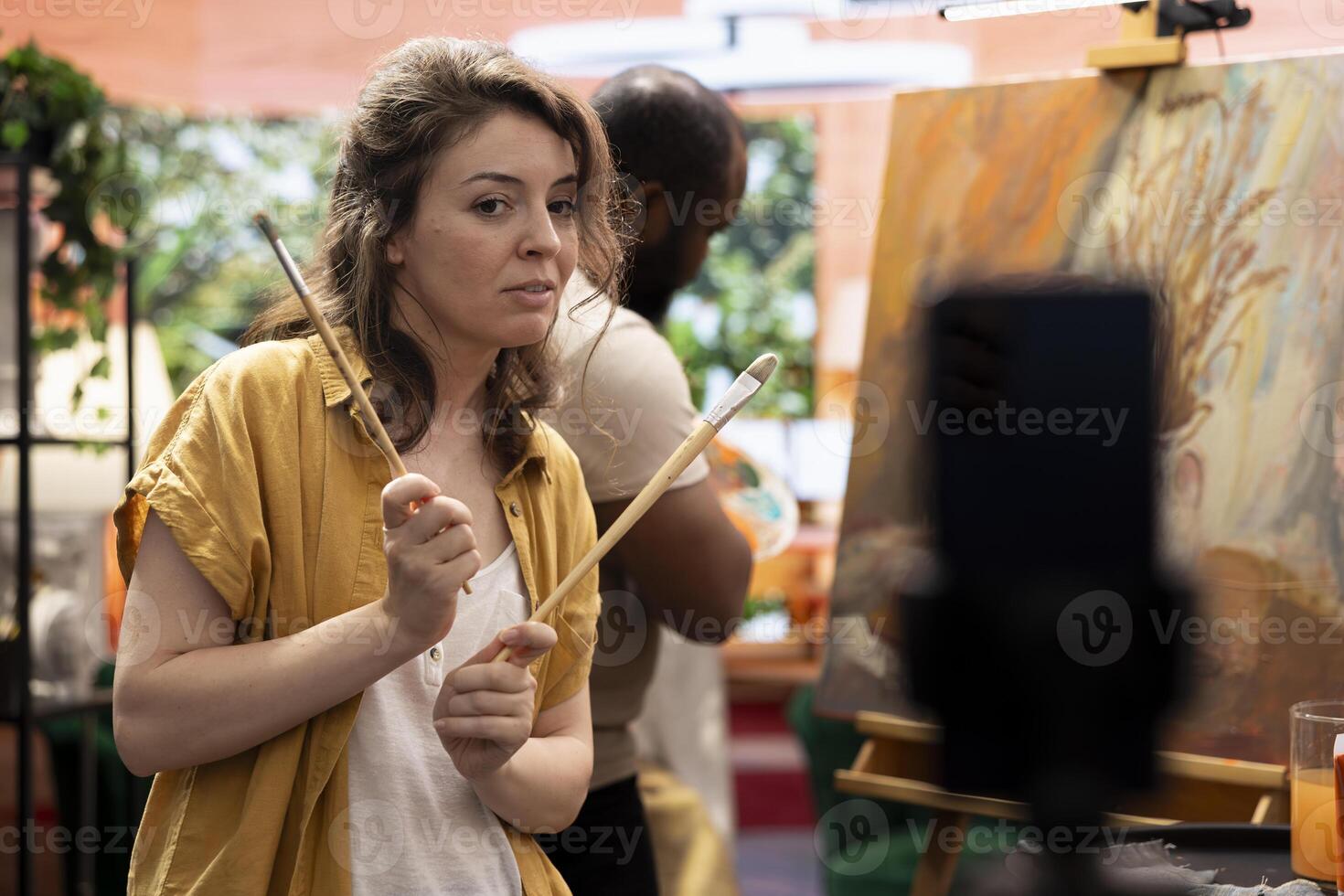 Woman painter filming demonstration during artistic creative process and explaining the painting technique used for an online e learning tutorial. Diverse team creating a vlog for virtual classroom. photo