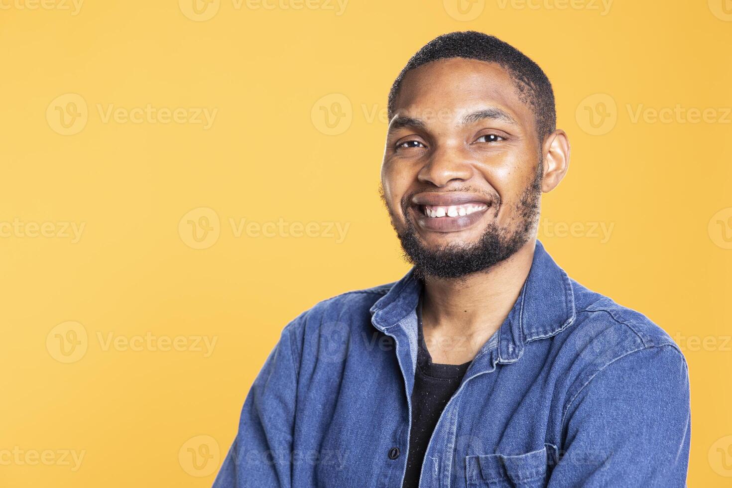Portrait of charming cool african american man posing on camera, standing with arms crossed against yellow background. Relaxed confident person in a good mood smiling in studio. photo