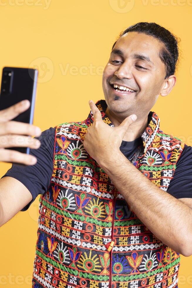 Cheerful man using cellphone to take selfies, rubbing chin. Smiling social media user taking photos using phone selfie camera, doing ego stroking hand gesturing, studio background