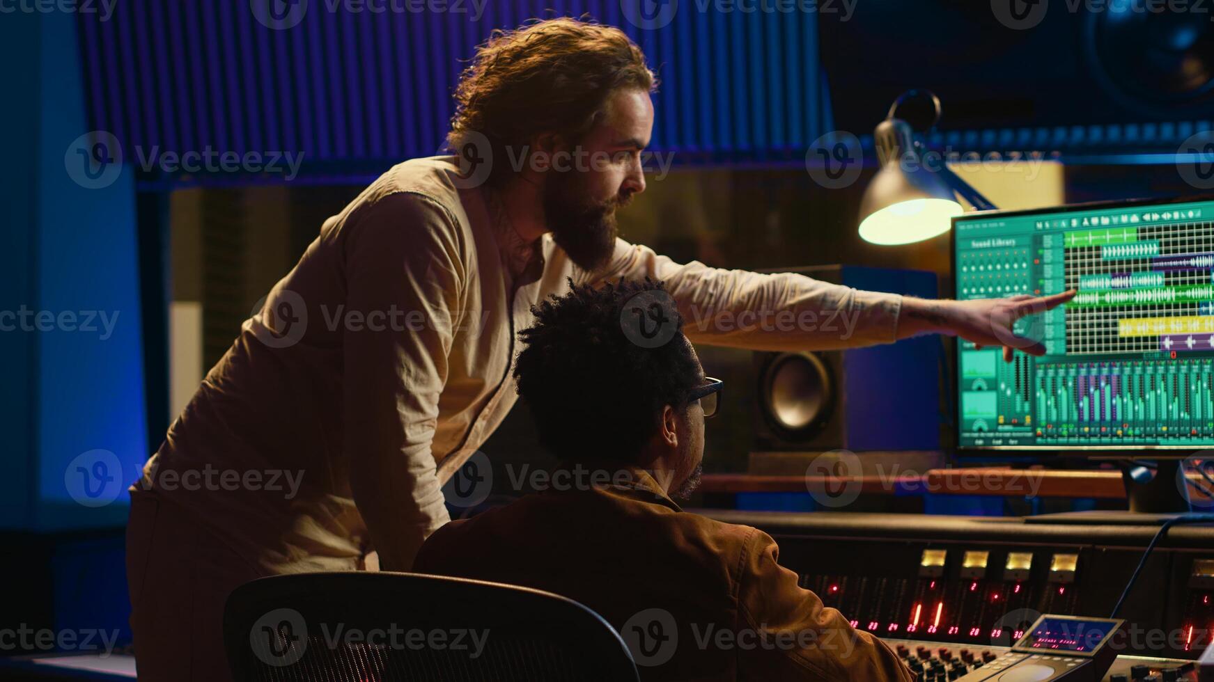 Tracking engineer collaborating with musician to edit sounds in studio control room, recording tunes to create a new album. Audio expert operating audio mixer and controller. Camera A. photo