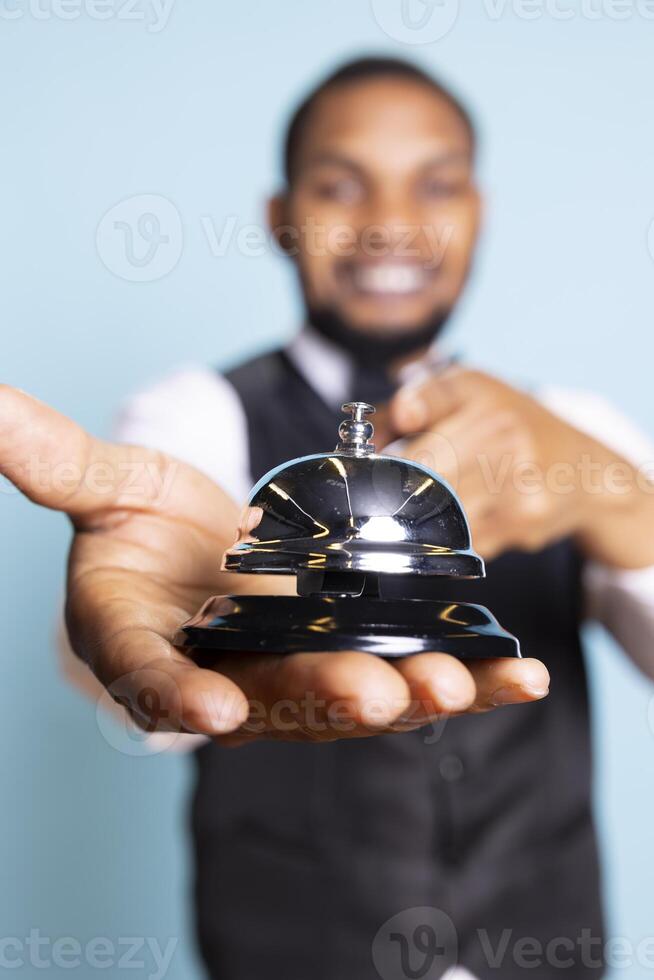 Bellhop doorkeeper ringing the service bell to present his help and assistance upon the guests arrival against blue background. Hotel porter providing great luxury services at resort. photo