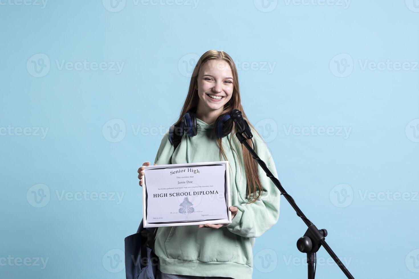 Happy student holding diploma talking in microphone, addressing audience, holding speech, studio background. Inspiring teenager using mic to share feeling during graduation ceremony photo