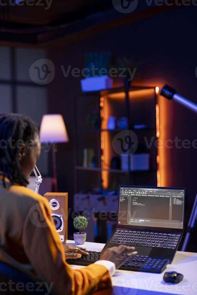 Computer scientist writes code on laptop screen while in apartment office using Java programming languages. African american teenager remotely working on fixing database errors photo