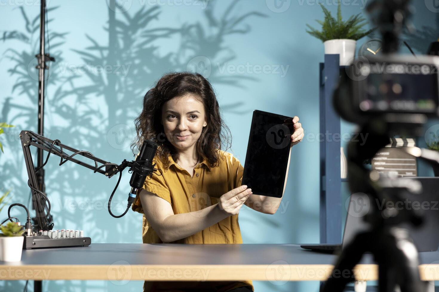 Smiling woman in studio filming tech tutorial on how to do maintenance on broken tablet. Cheerful technology internet show host teaching subscribers how to open and fix digital device photo