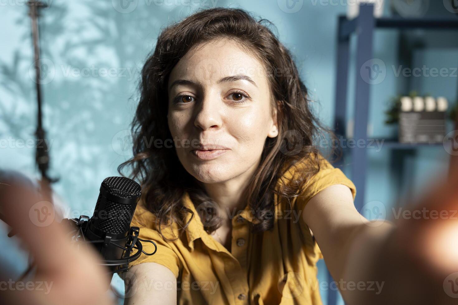 Woman filming vlog with selfie camera in professional studio, speaking into microphone equipment. POV shot of upbeat influencer talking to subscribers about trending topics on online channel photo