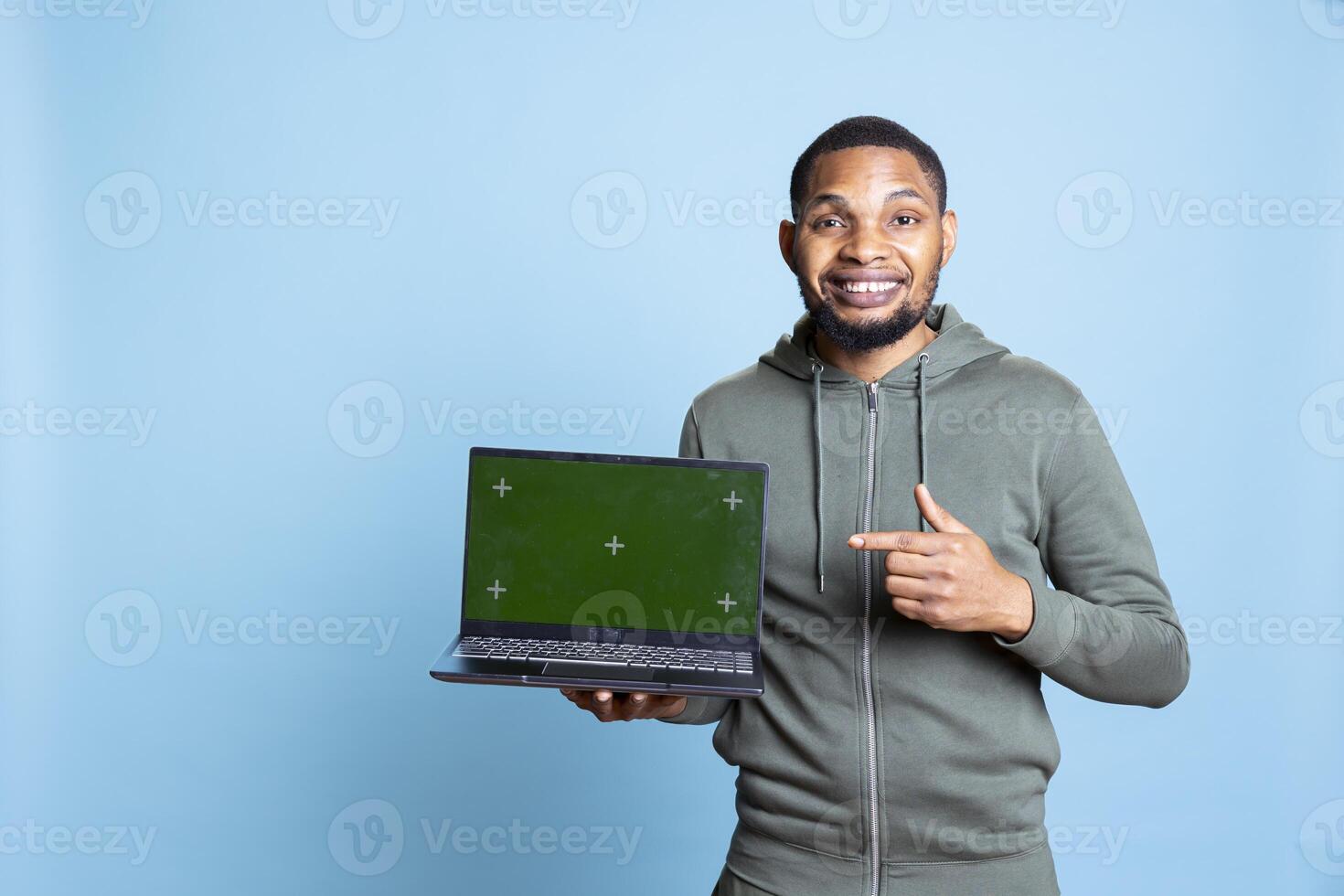 Jolly african american person presenting green screen display on laptop, doing recommendation. Friendly young guy pointing at mockup on notebook, wearing casual clothes in studio. photo