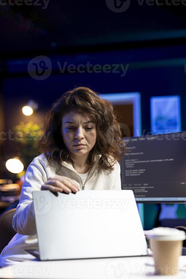 IT expert working from home, opening laptop, testing and deploying programs and systems. Engineer checking code displayed on computer monitors, sitting at desk chair in apartment photo