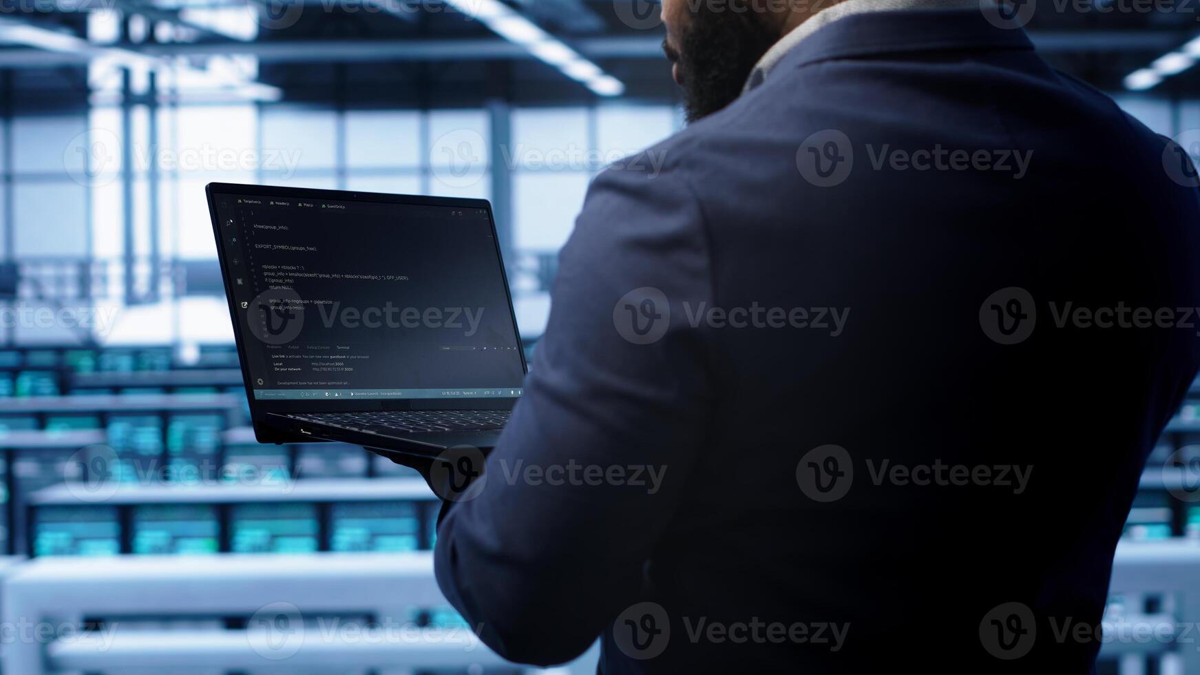 Programmer doing yearly maintenance checkup using laptop to prolong data center electronics life span. IT professional in server farm monitoring server infrastructure using notebook, camera A photo