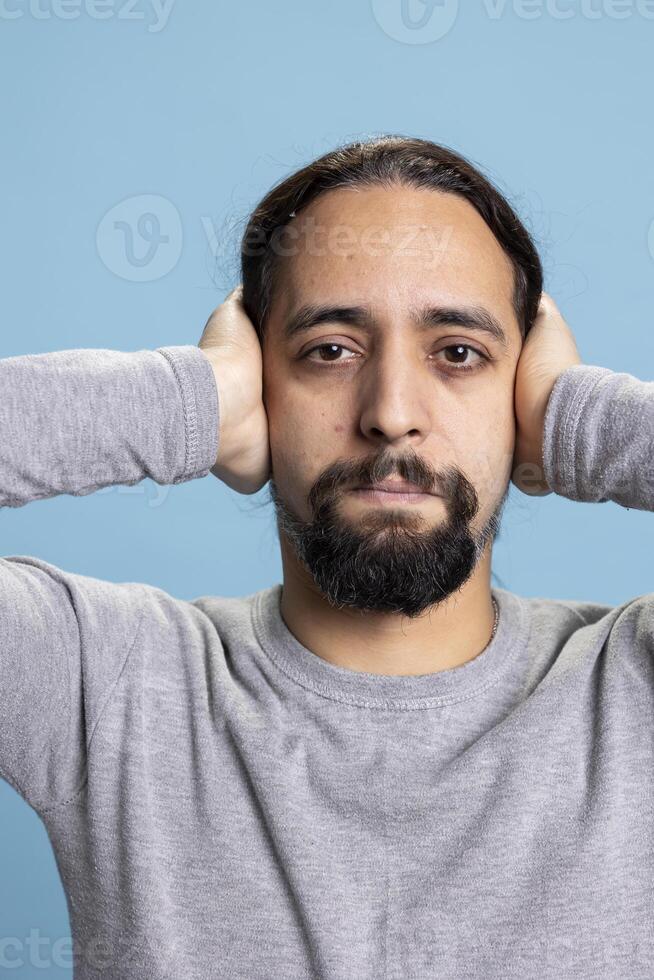 Serious moral adult covering his ears as part of the three wise monkeys illustration, showcasing the ethic motivational idiom on camera. Young man hearing no evil with traditional wisdom concept. photo