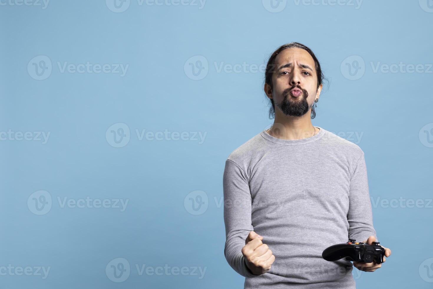 Overjoyed young adult winning an online tournament in the studio, feeling pleased and proud of his victory against blue background. Satisfied guy smiling in front of camera, games on console. photo