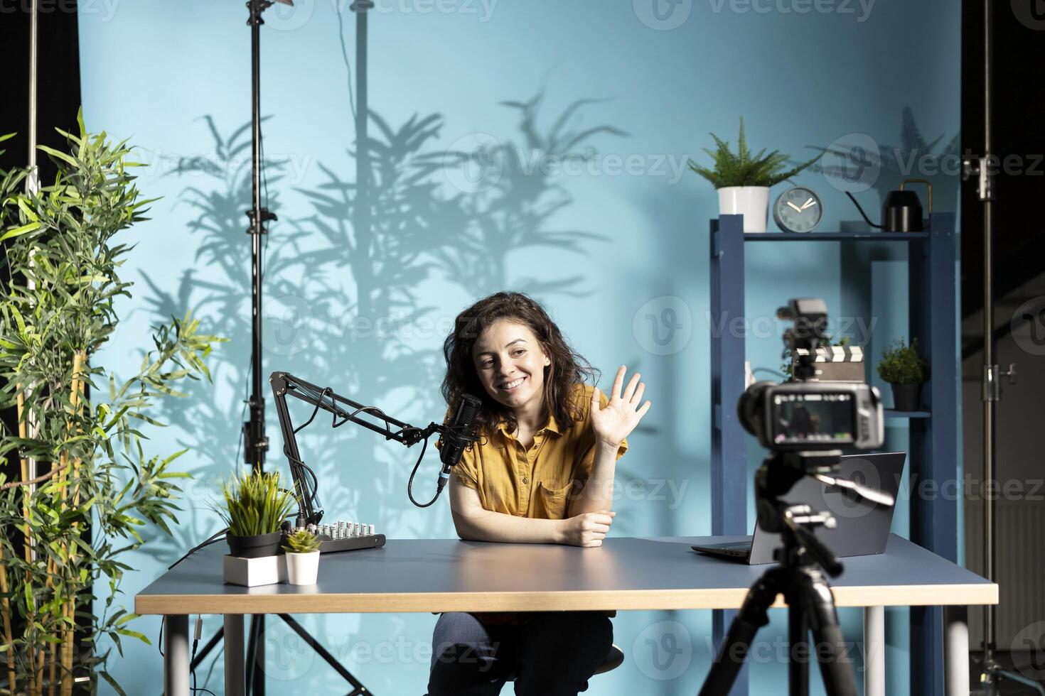 Jolly woman greeting fans, filming vlog with high tech gear in professional studio, speaking into microphone equipment. Smiling influencer saluting subscribers, talking about trending topics on online channel photo