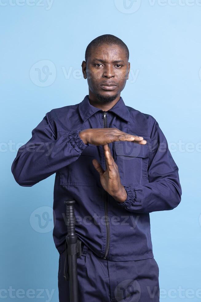 African american security officer showing a timeout sign to take a break from his long shift, experiencing burnout and working under pressure. Serious unhappy guard asking for a pause. photo