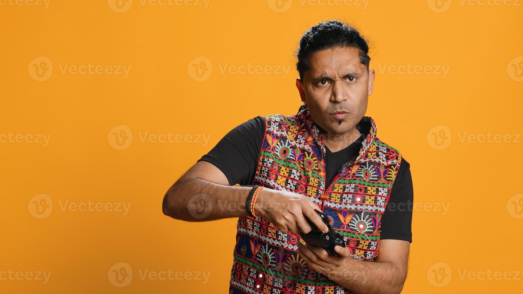 Cheerful man playing videogames with controller, studio background. Indian gamer smiling, having fun by participating in PvP online multiplayer game using console system, camera A photo