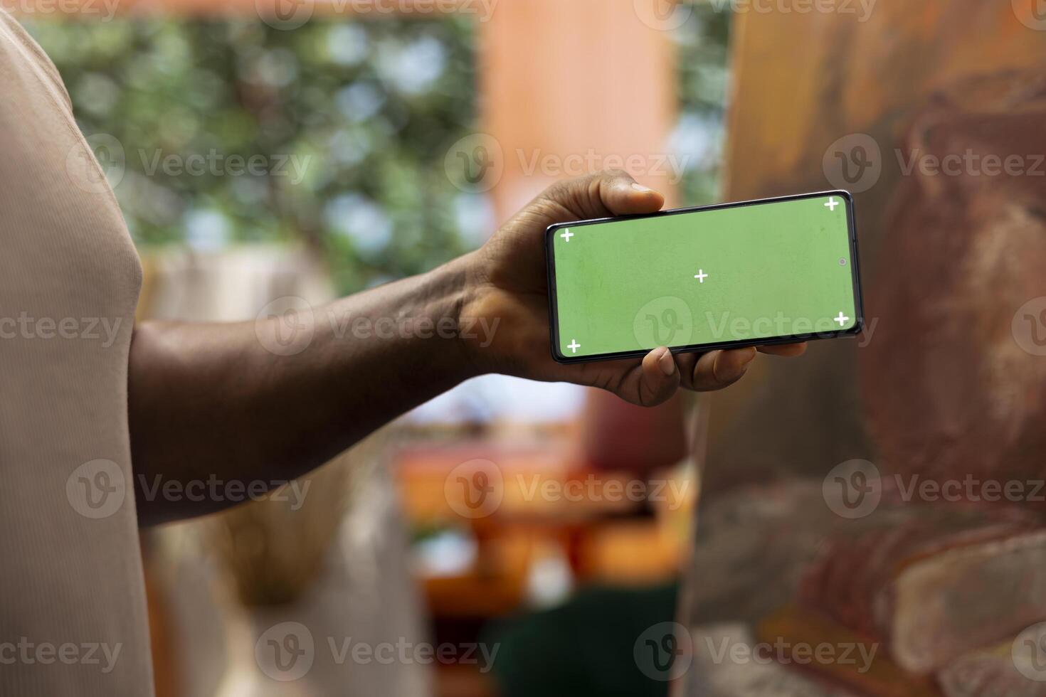 Young artist looking at isolated chroma key display in his painting atelier, using device next to canvas with a colorful masterpiece. Painter creating a rustic artwork for the gallery exhibition. photo