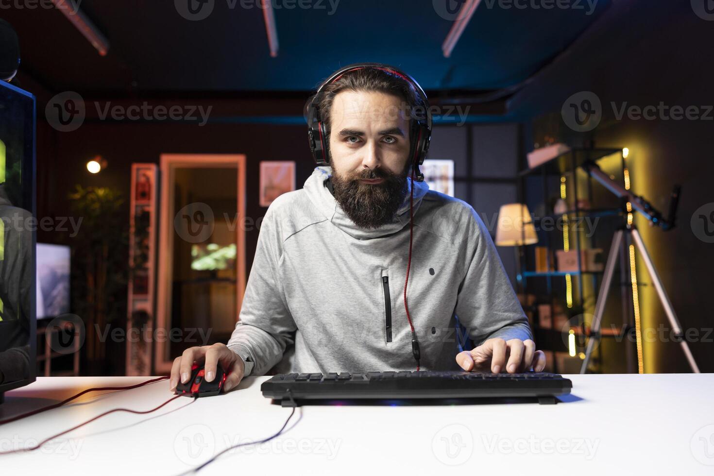 Content creator wearing headphones chatting with audience while playing online multiplayer videogame on PC, contending against players. Pro gamer broadcasting game on internet, talking in headset mic photo