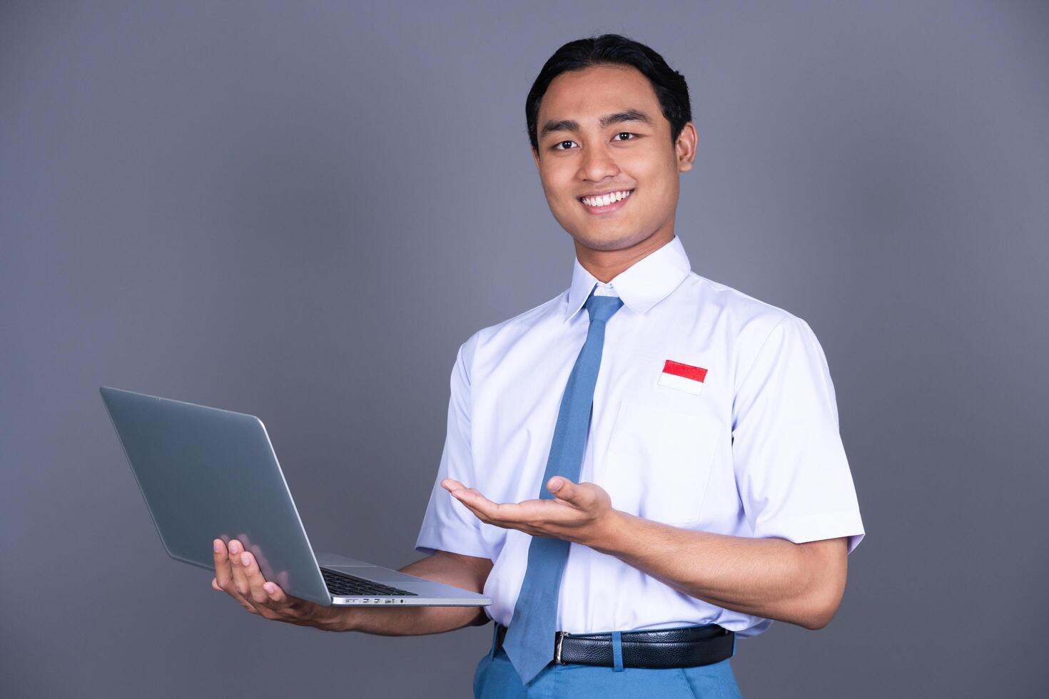 Indonesian Male High School Student in Uniform Smiling While Holding a Laptop Isolated Background photo