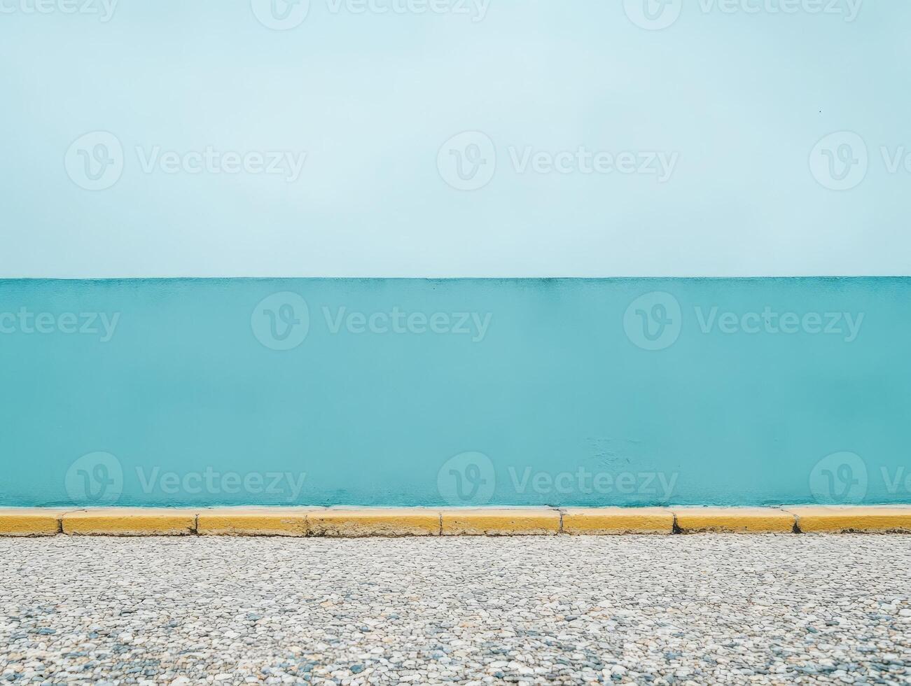 A minimalist scene featuring a blue wall against a gravel surface and a yellow curb. photo