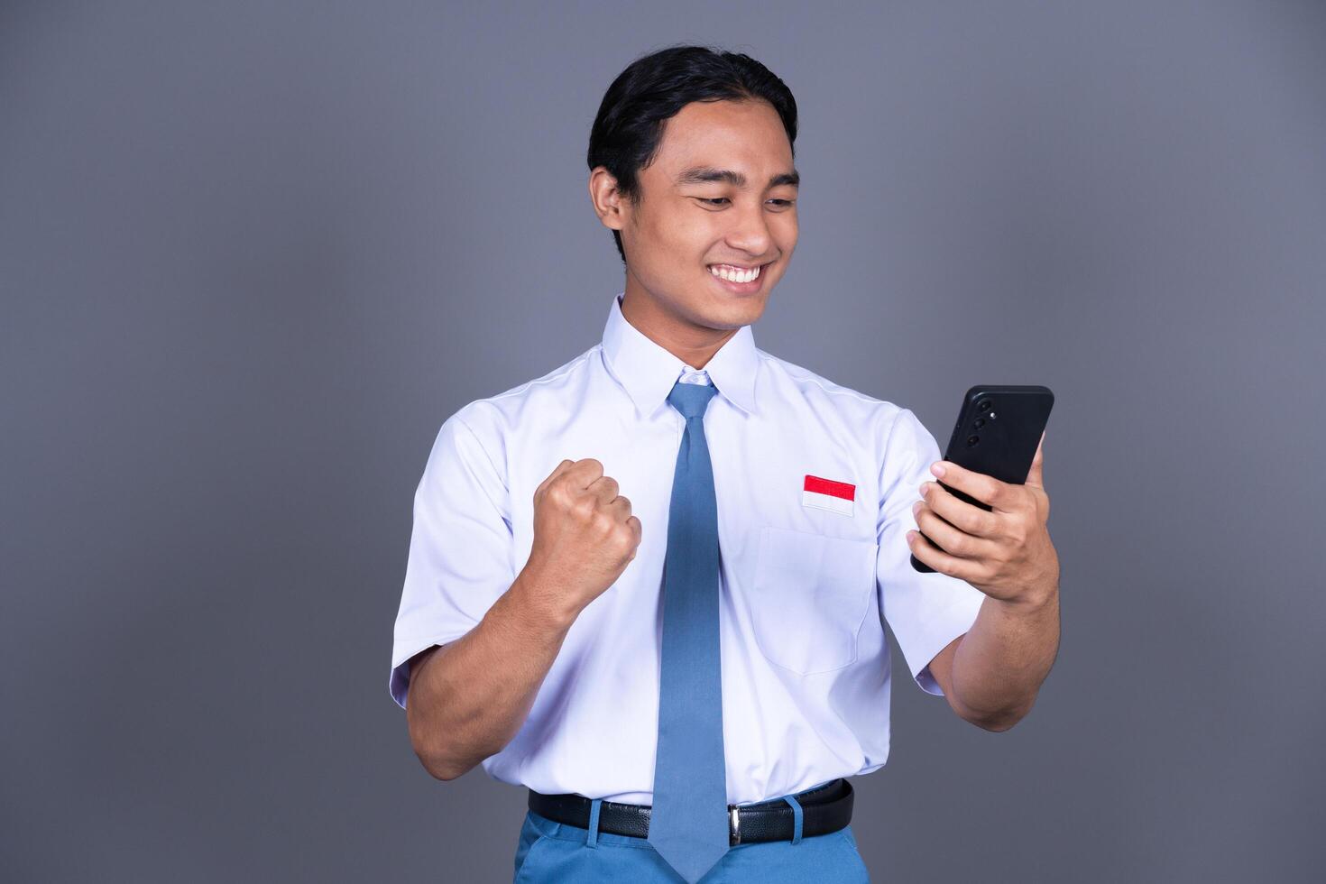 Indonesian Male High School Student in Uniform Smiling While Holding Phone And Shouting Yeah photo