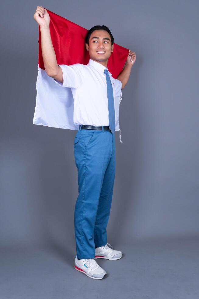 Indonesian Male High School Student in Uniform Waving Indonesian Flag Isolated Background photo
