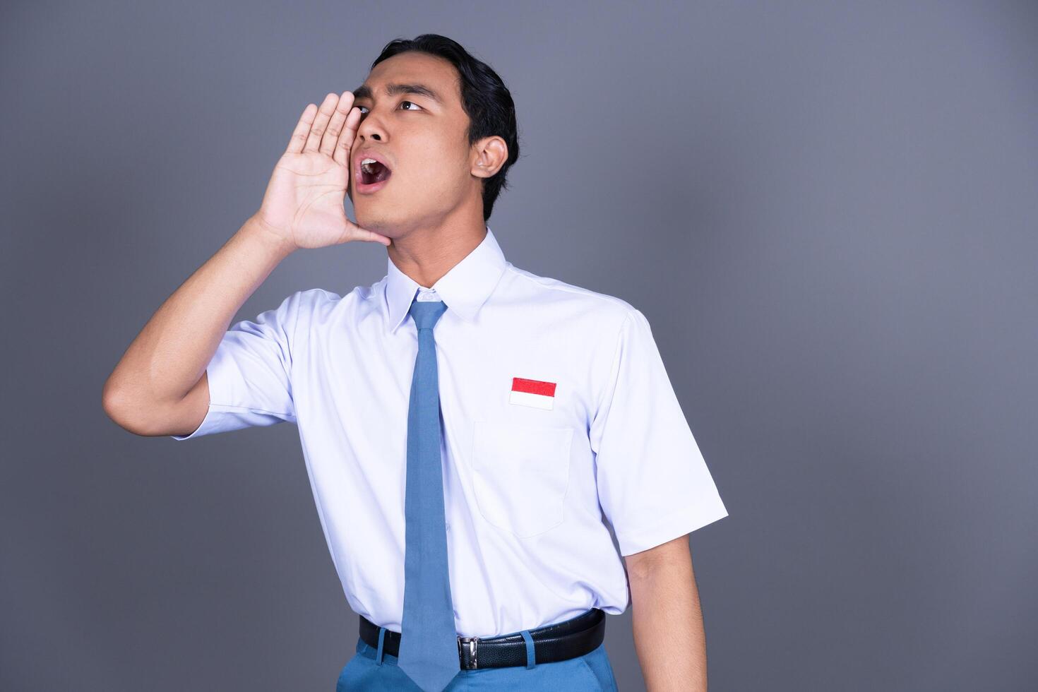 Indonesian Male High School Student in Uniform Shouting with Hand on Mouth Right Side photo