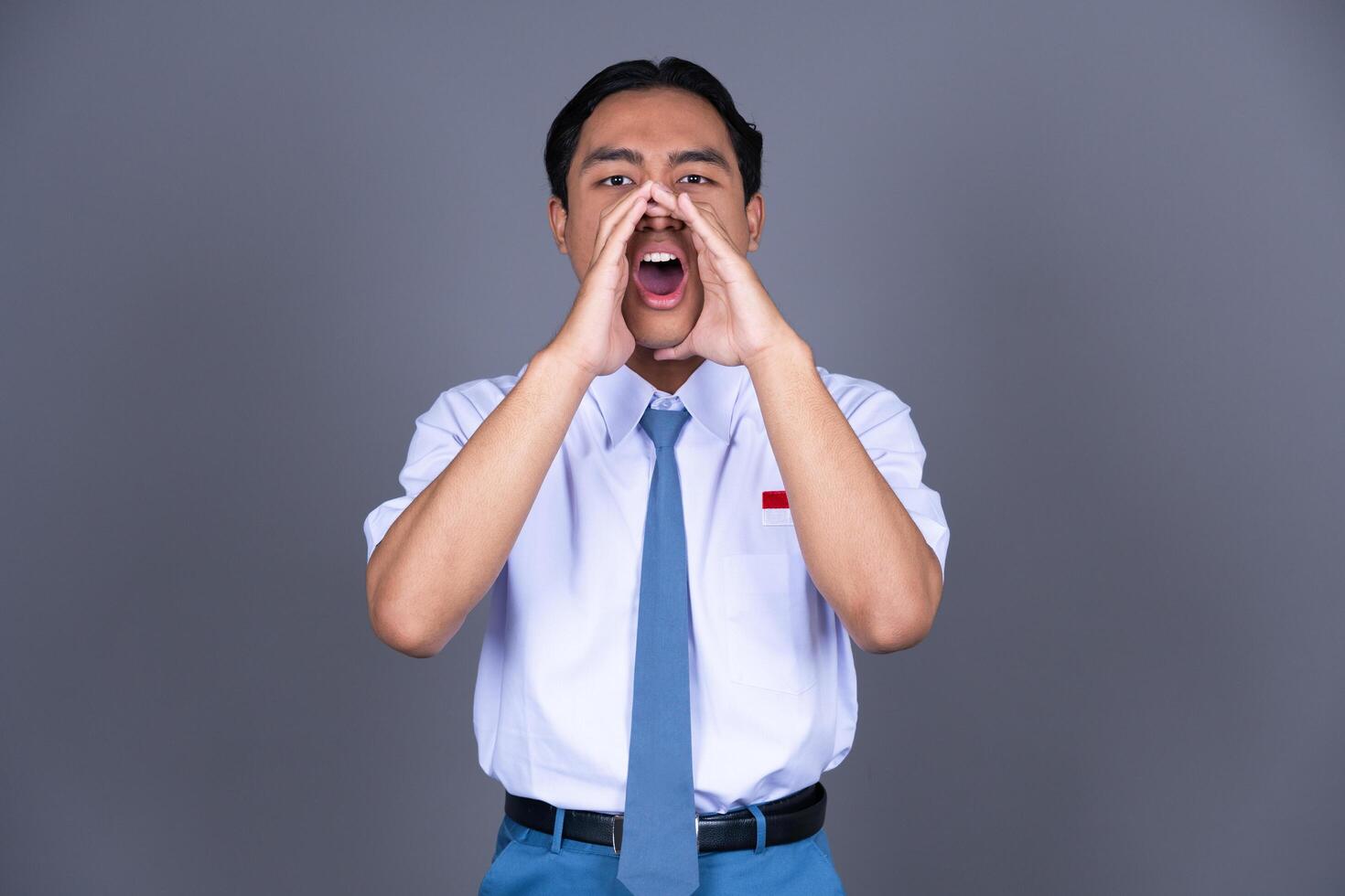 Indonesian Male High School Student in Uniform Shouting with Hand on Mouth Isolated Background photo