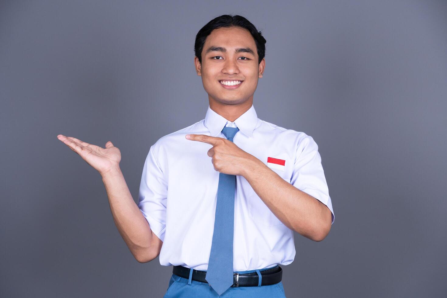 Indonesian Male High School Student in Uniform Smiling While Pointing Finger Background photo