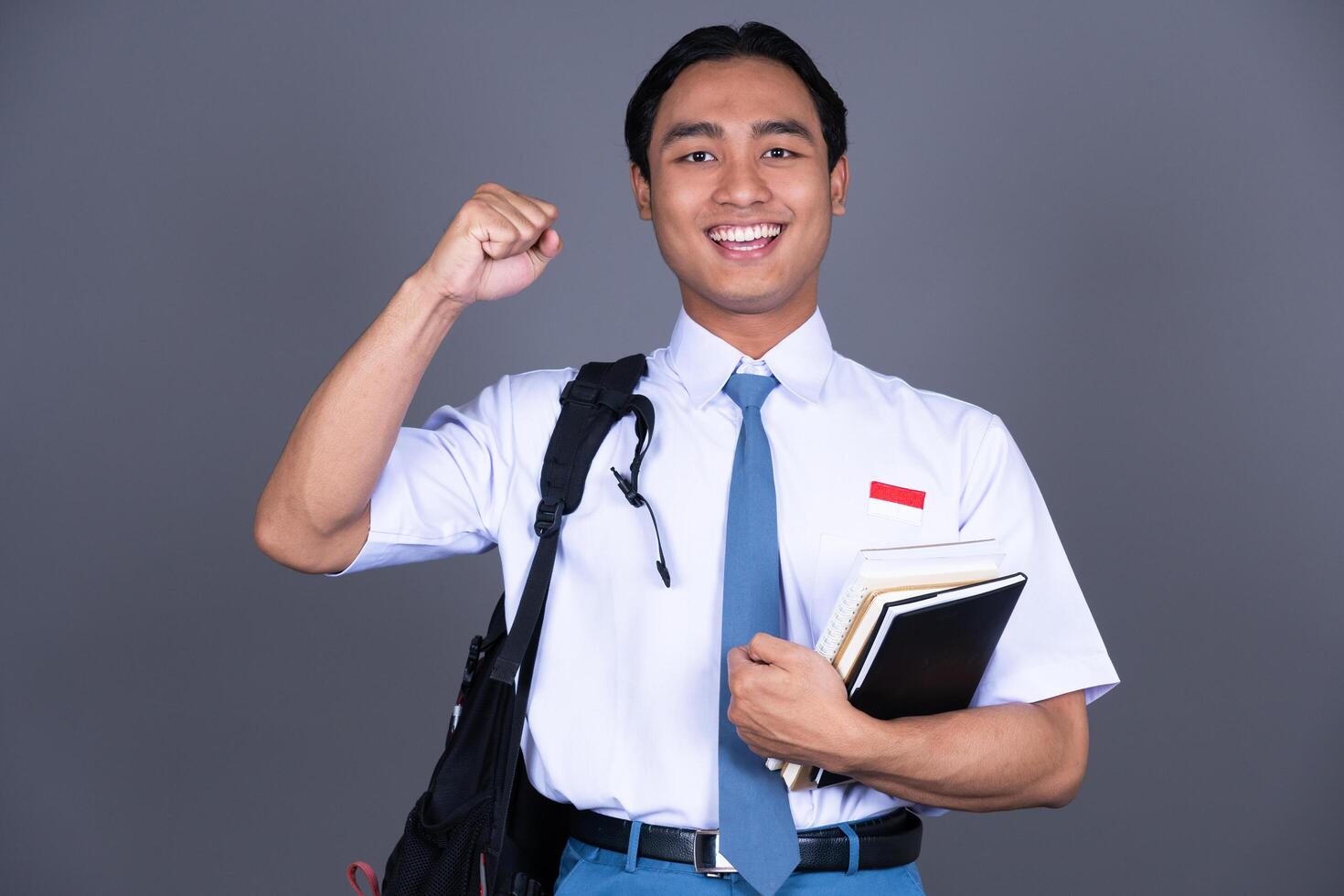 Indonesian Male High School Student in Uniform Gesture Celebrating and Carrying Books photo