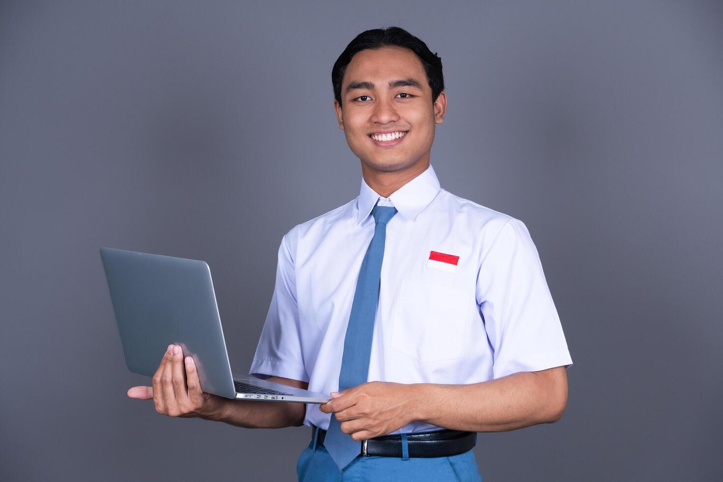 Indonesian Male High School Student in Uniform Smiling While Holding a Laptop And Smiling photo