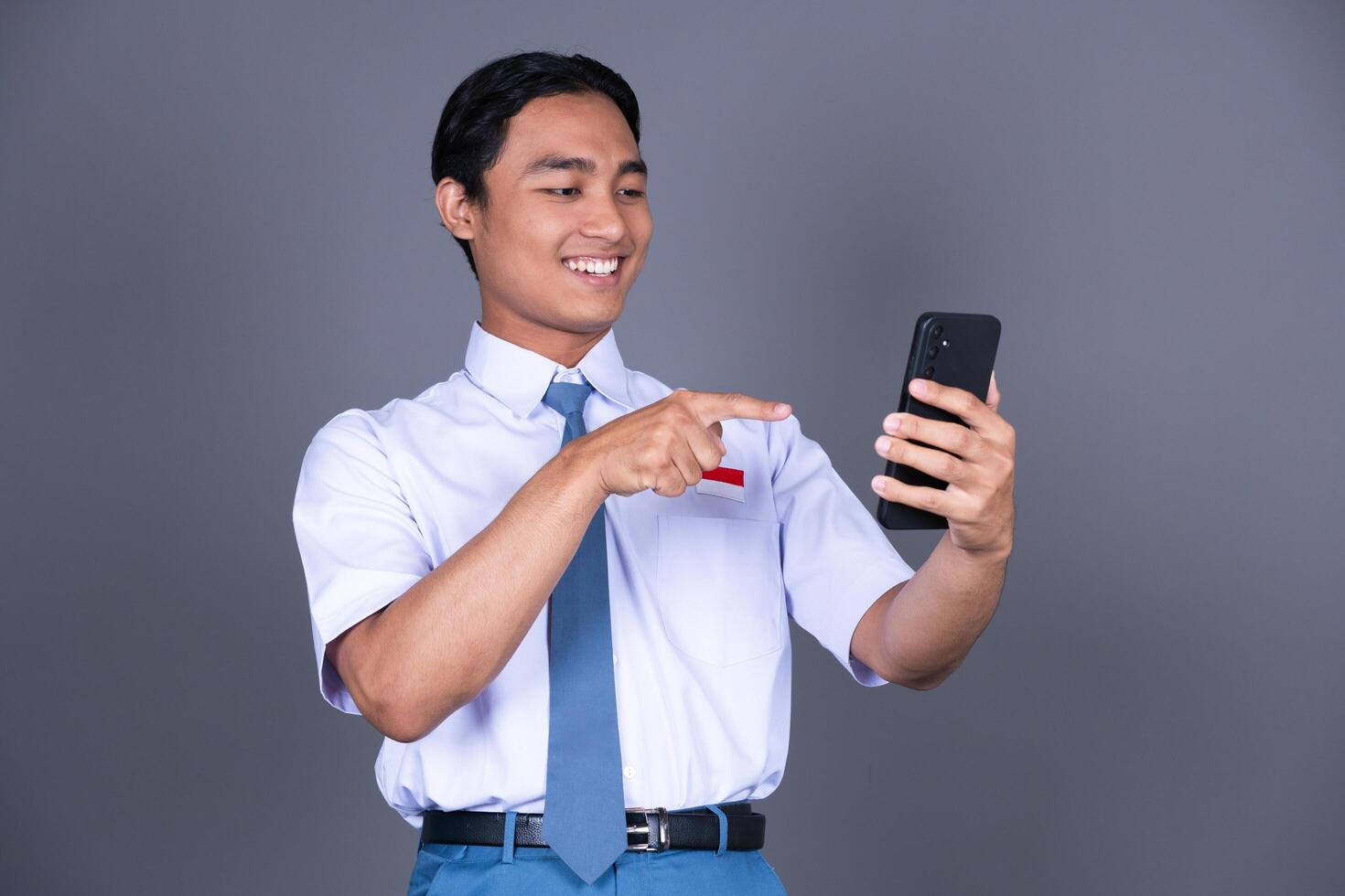 Indonesian Male High School Student in Uniform Smiling While Holding Phone Isolated Background photo