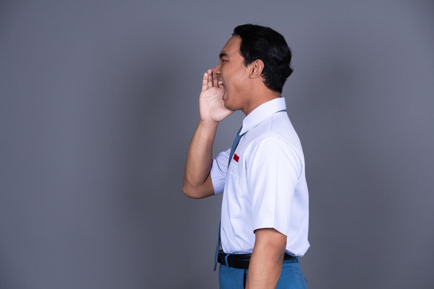 Indonesian Male High School Student in Uniform Shouting with Hand on Mouth Background photo