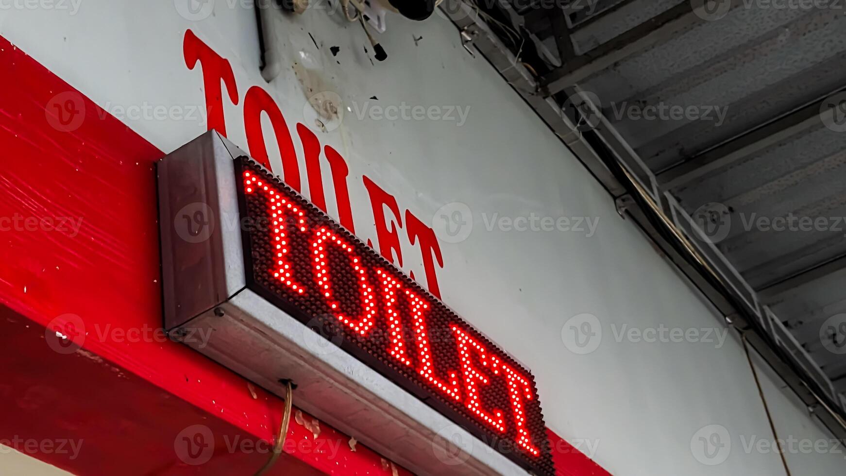Bright red LED sign displaying 'TOILET' on a wall with a matching painted label. The image captures a modern restroom indicator in a public space, highlighting clear signage and direction. photo