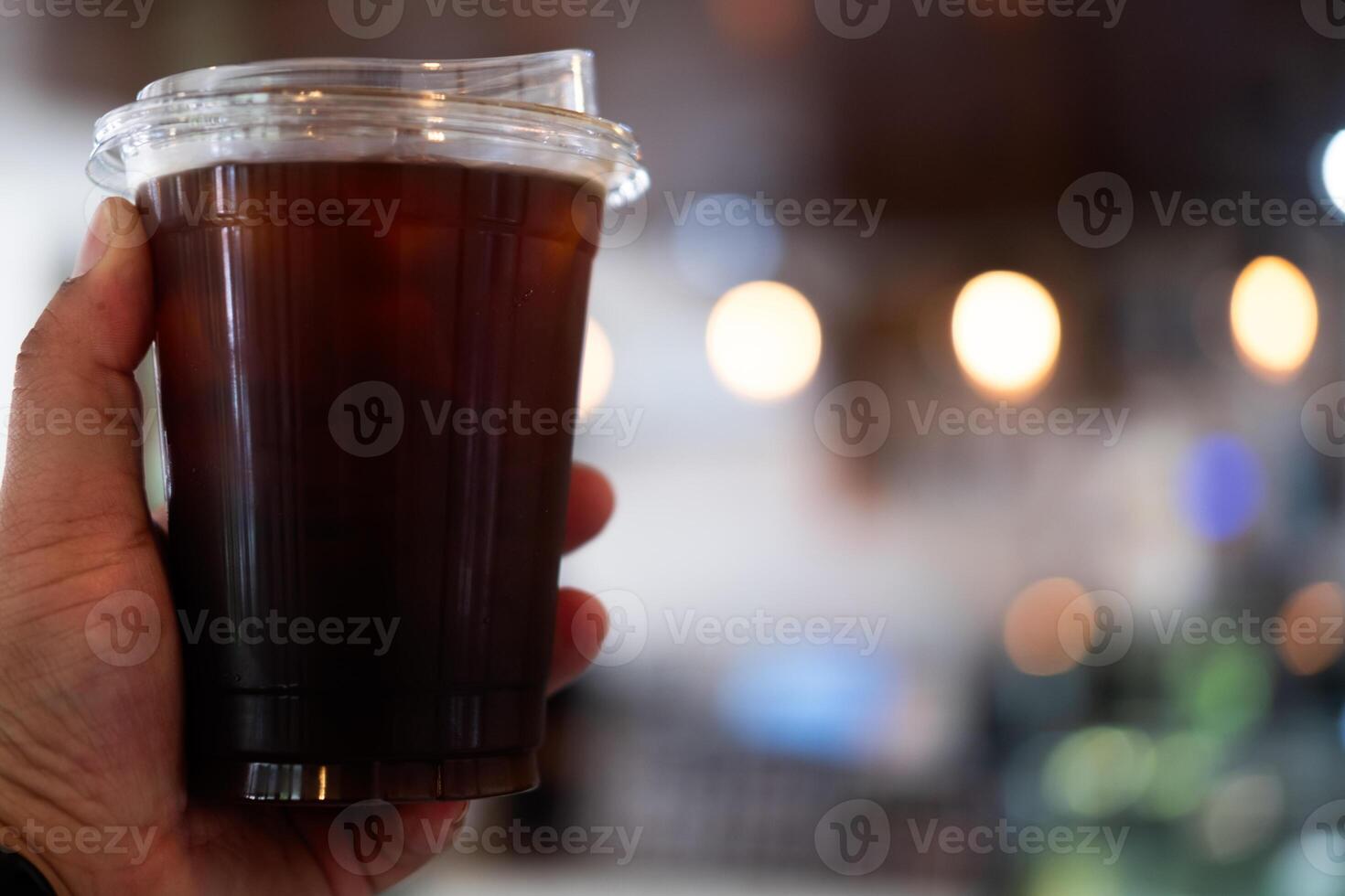 Hand holding a take away plastic cup of Iced black coffee. photo