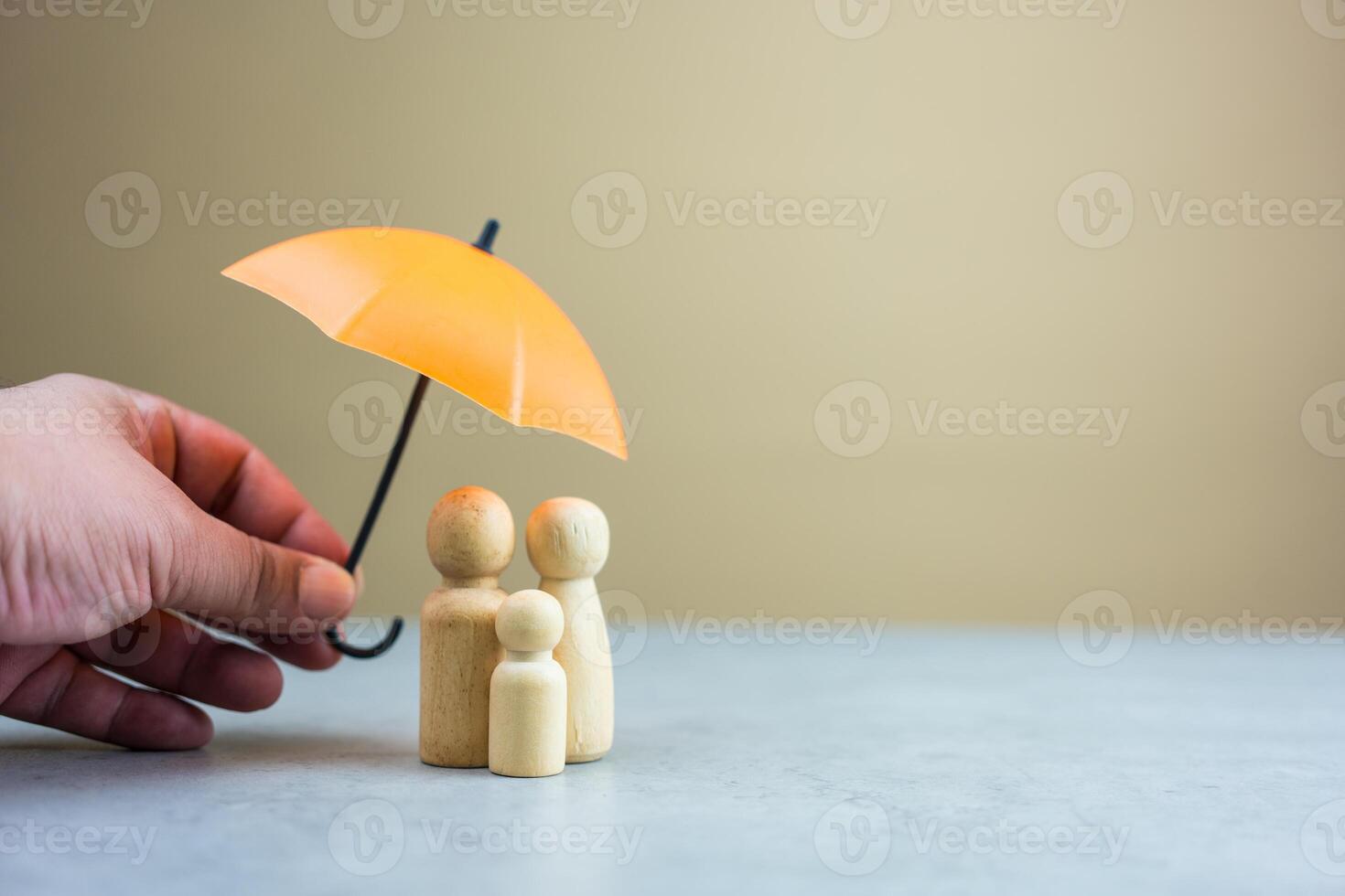 Someone hand holding orange umbrella protects a family of wooden peg dolls. Insurance concept. photo