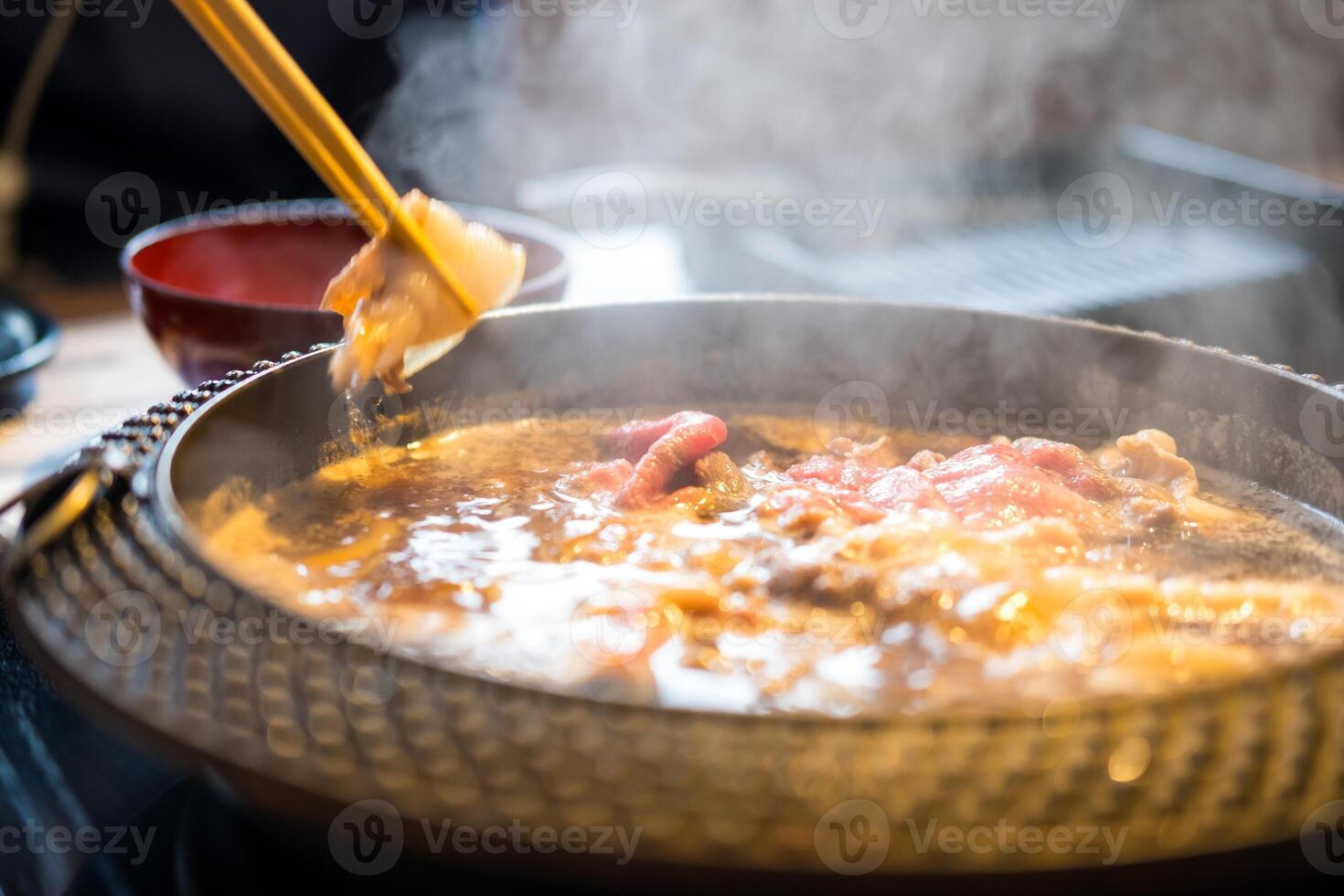 Holding sliced pork using chopsticks on hot pot with smoke for Japanese hot pot photo
