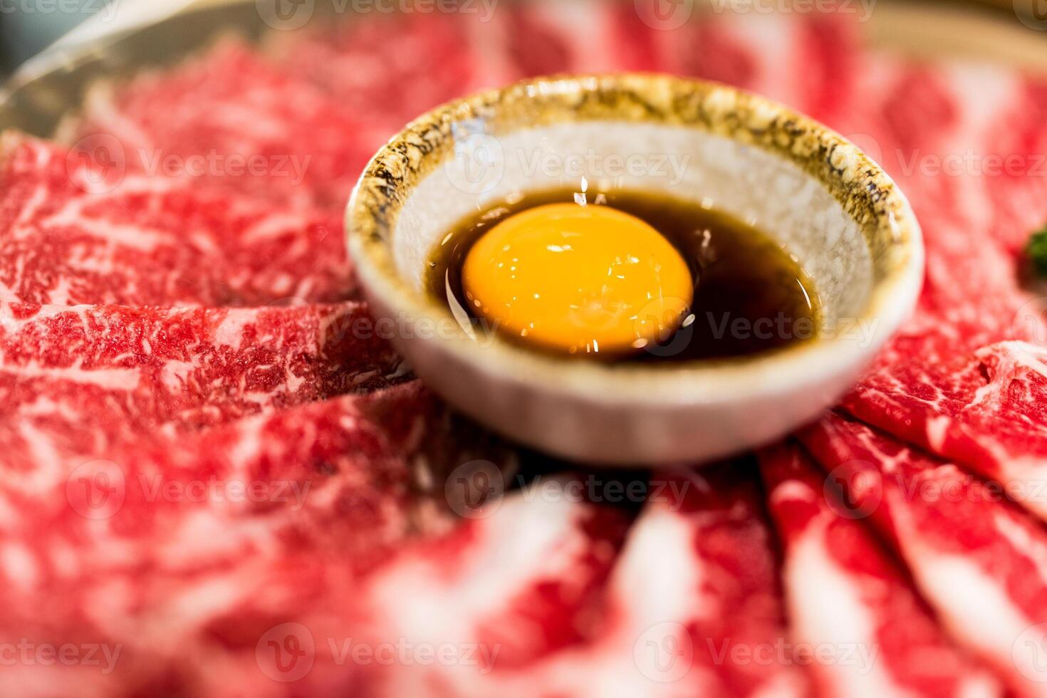 Sliced raw beef arranged on a plate with a raw egg yolk centerpiece for sukiyaki. photo